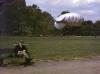 A man sits on a park bench in London, reading a book. Also a moored "barrage balloon" is visible in the background, while a second one soars high in the distance.