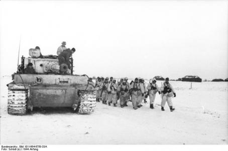 Tiger I tank accompanying infantry column marching in white camouflage on a snowy road.