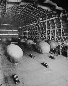 British barrage balloons stored in a hangar tied to trucks.