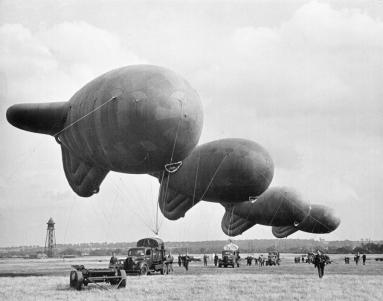 British barrage balloons in a field tied to trucks.